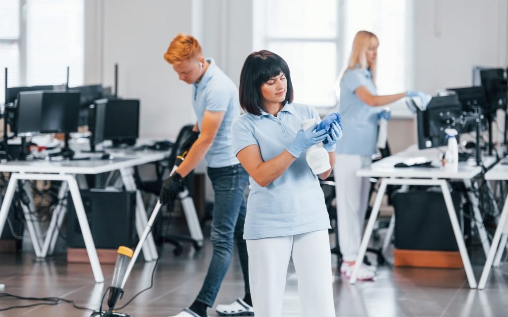 Cleans floor. Group of workers clean modern office together at daytime Cleans floor. Group of workers clean modern office together at daytime